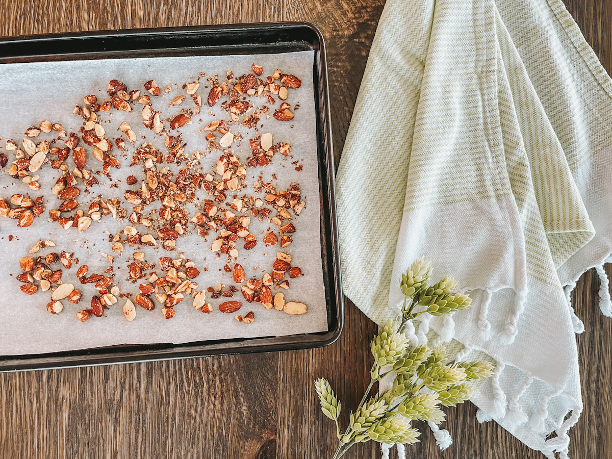 toasted almonds on top of parchment paper on a sheet pan next to a green striped dish towel 