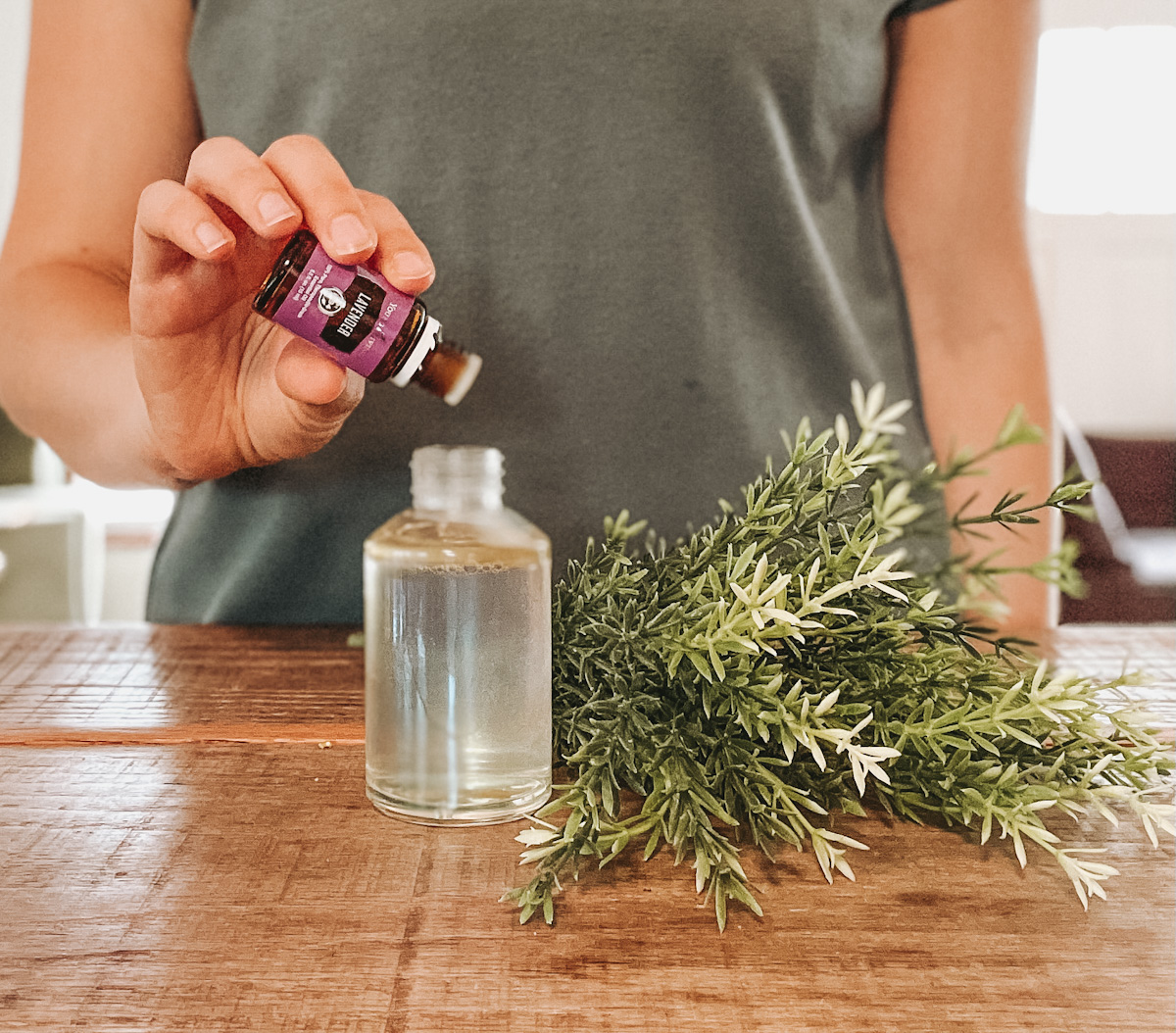 woman refilling diy hair growth spray bottle with lavender essential oil on a wooden countertop