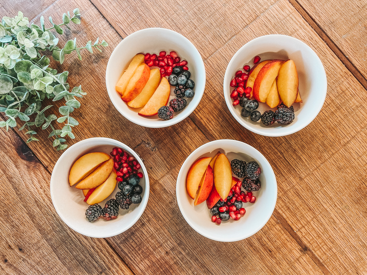 four kid's snack bowls filled with a variety of fruits on a wooden countertop