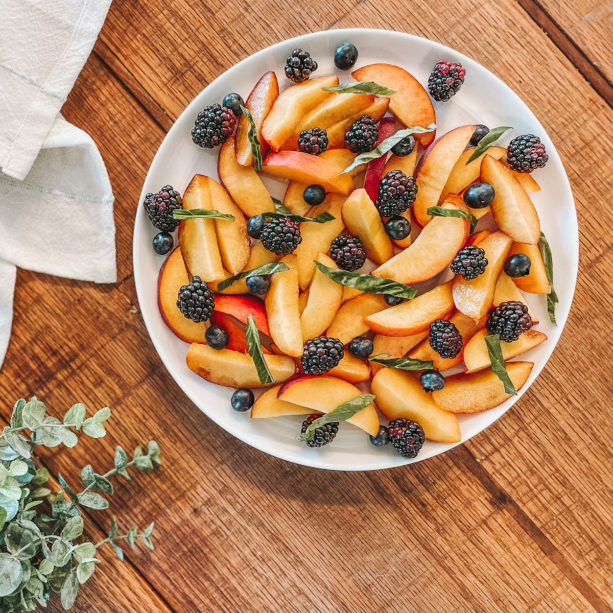 peach fruit salad with honey lime dressing on a white plate on a wooden countertop