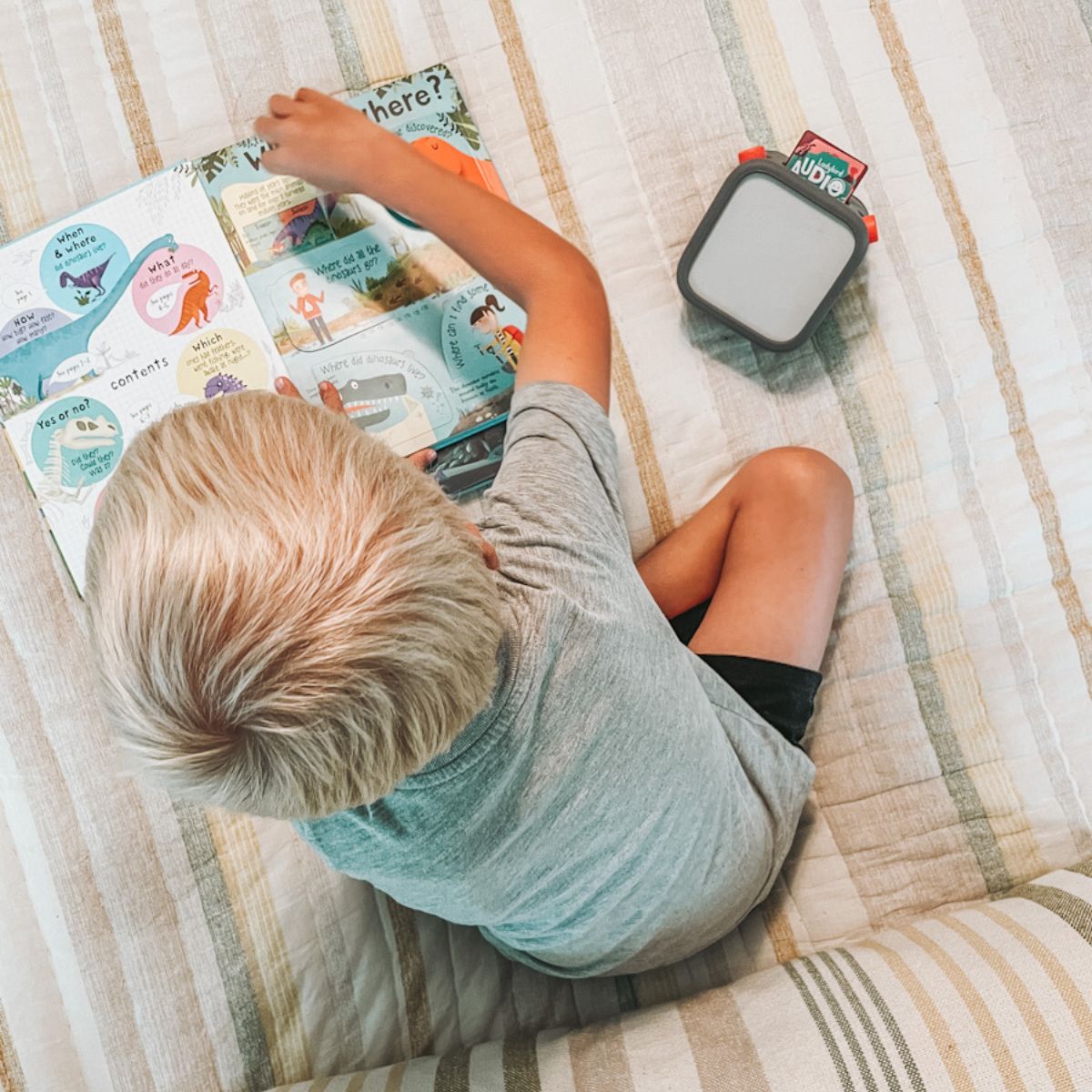kid in quiet time sitting on bed with a book and Yoto player audiobook
