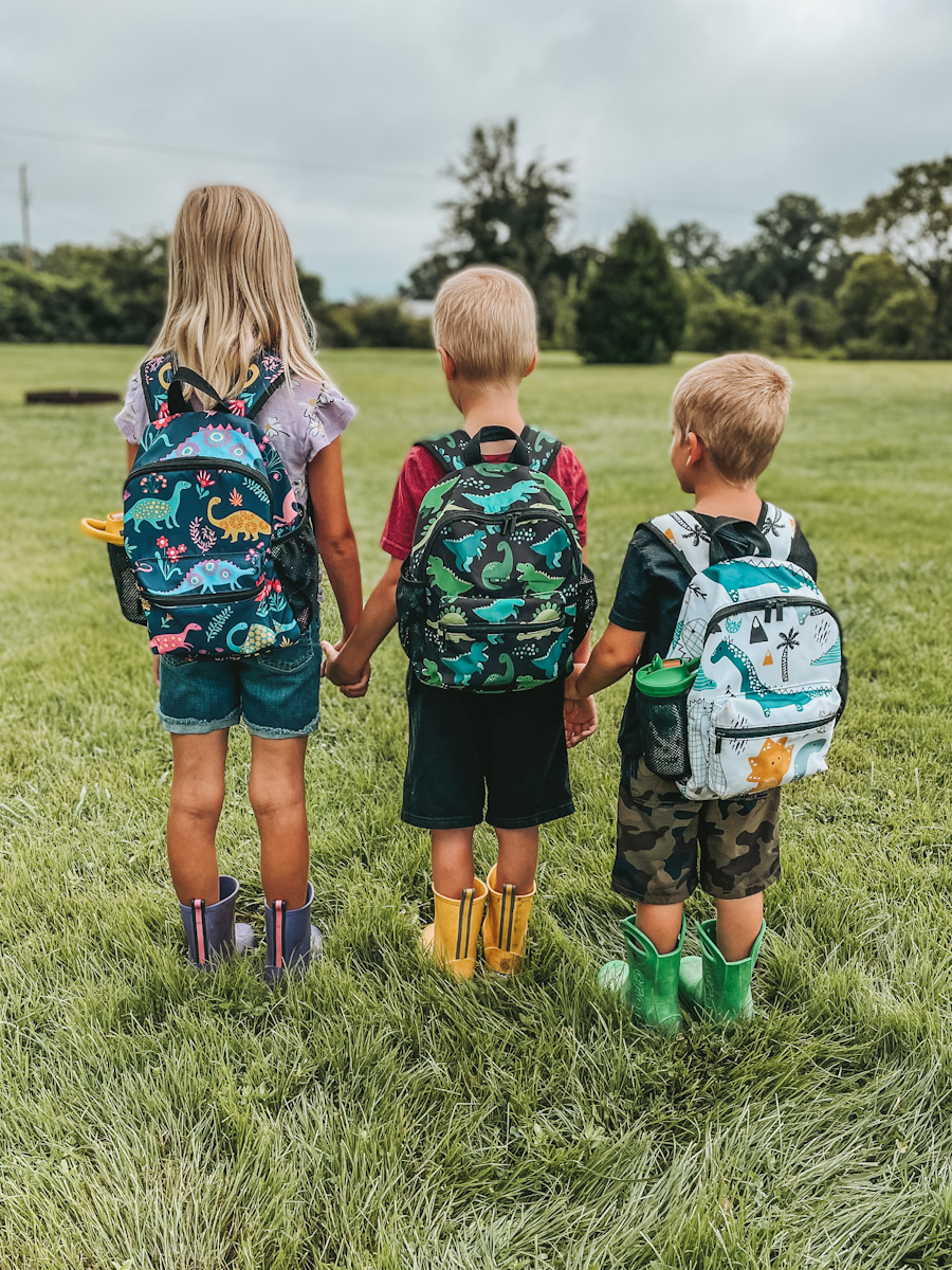 three kids wearing backpacks to hold all of the outdoor essentials for nature exploring