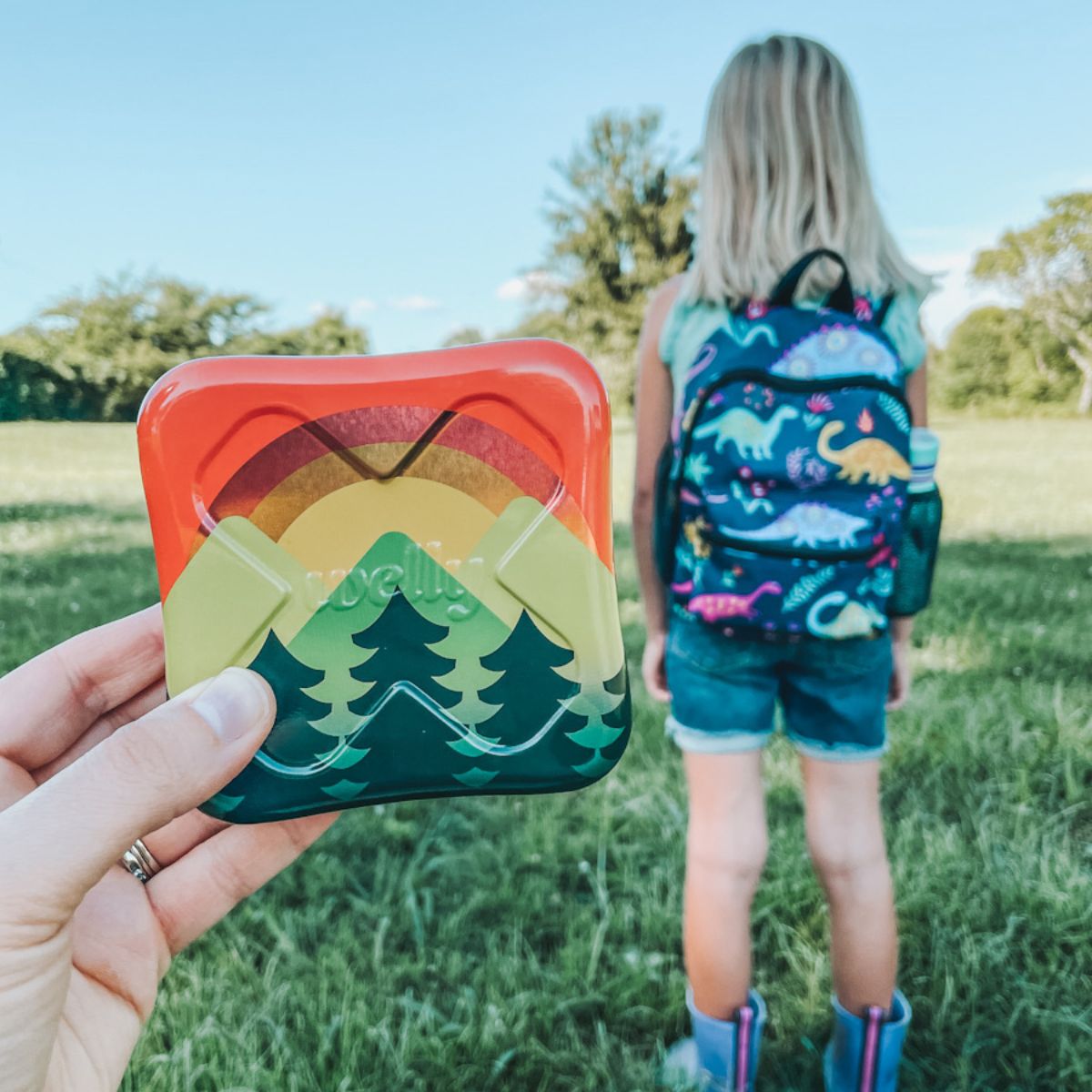 refillable first aid kit being held up in front of a girl with a backpack on
