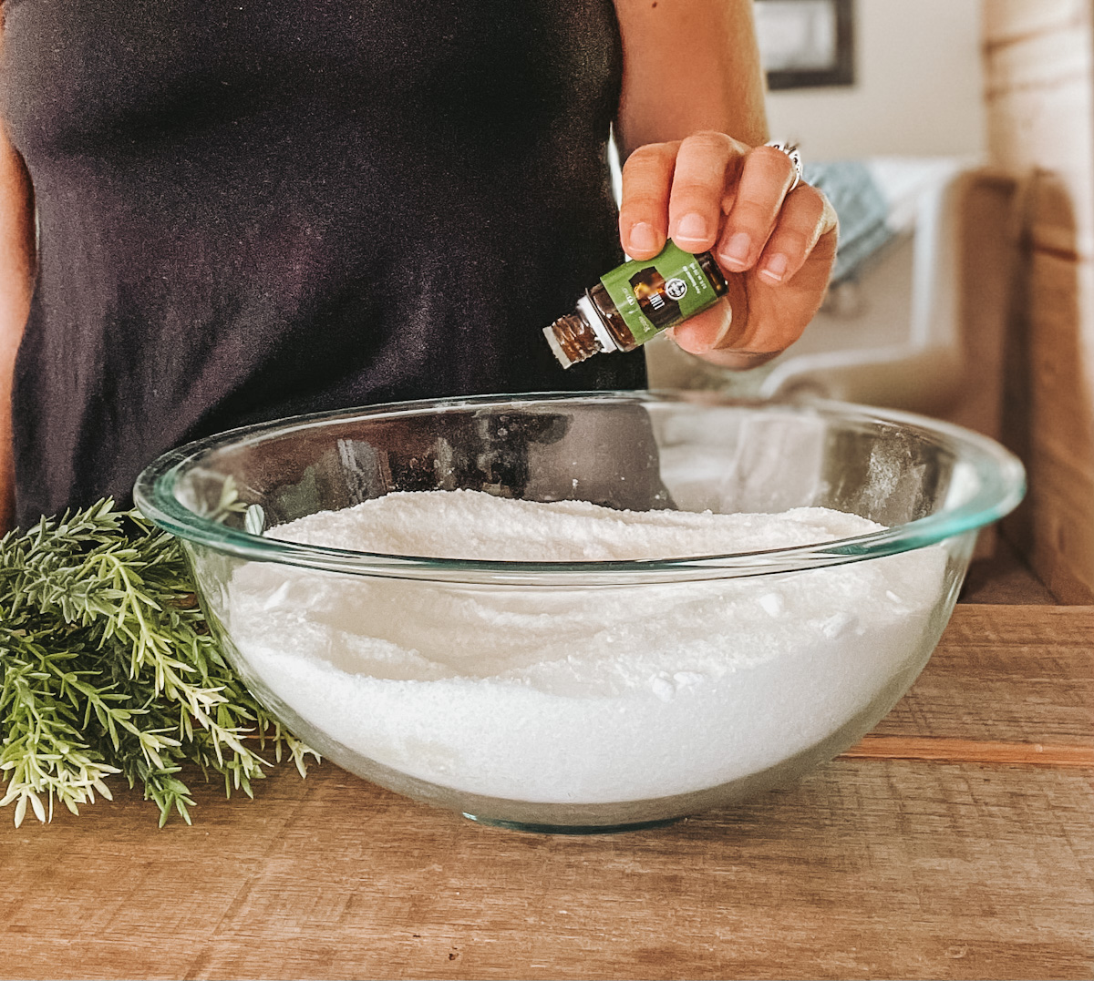 Lime essential oil being dropped into a large glass bowl filled with Epsom salt and baking soda