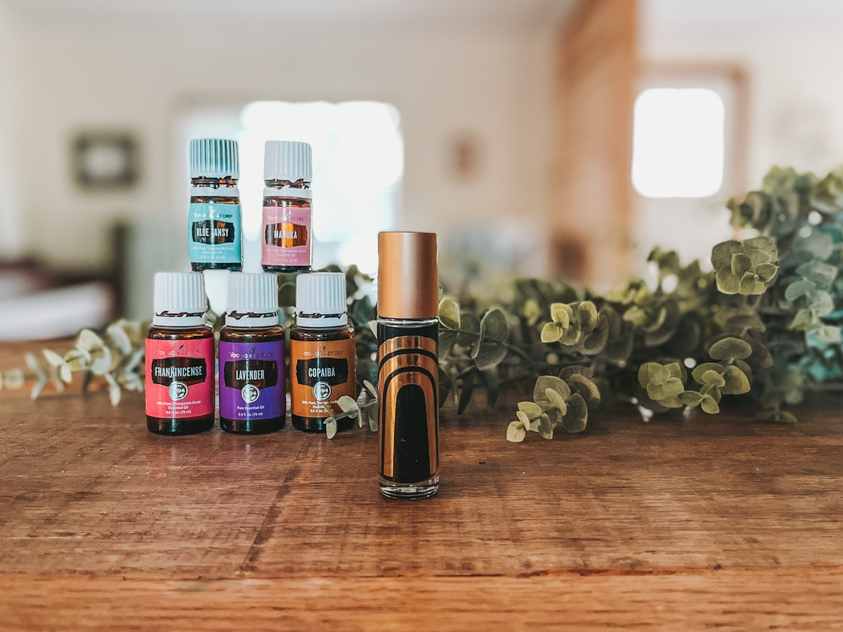 best face serum for glowing skin essential oil roller bottle standing up on a wood countertop in front of essential oils