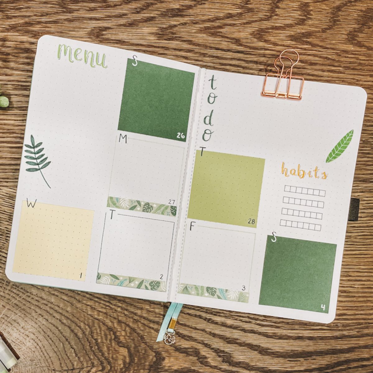 green themed bullet journal weekly spread laid out on a wood tabletop, includes a menu, habits, to do list and days of the week