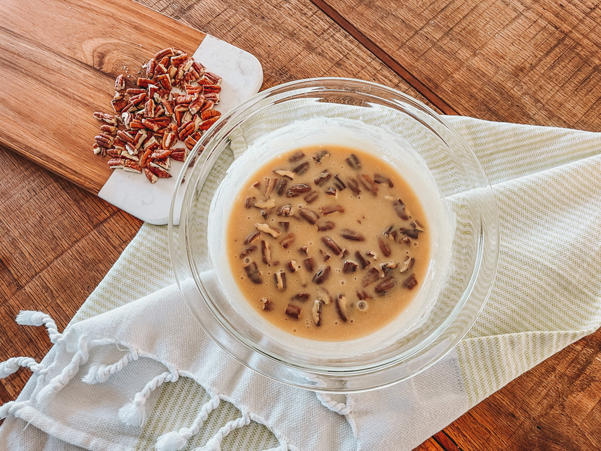 condensed milk caramel in a glass bowl with chopped pecans mixed in and set on the counter to cool