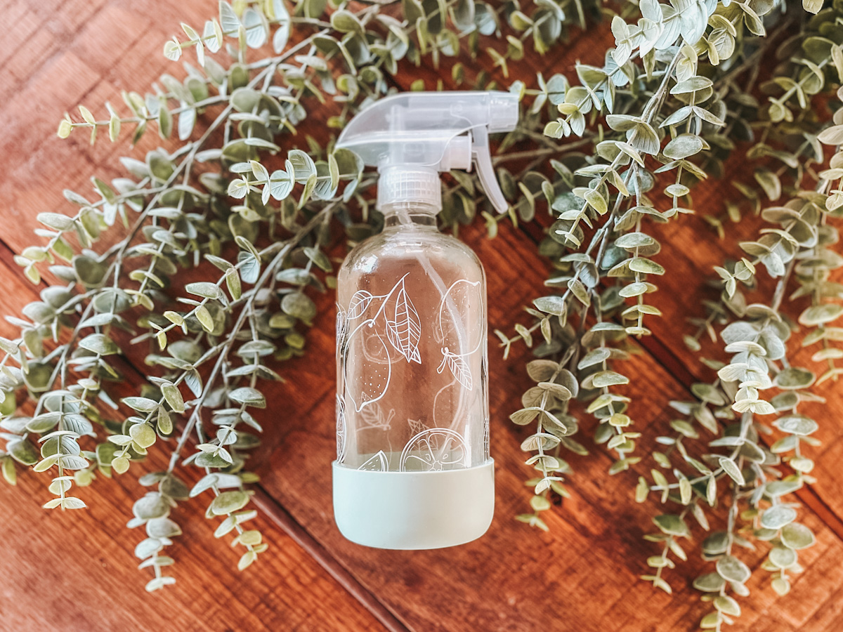 non toxic all purpose cleaner in a glass spray bottle laid out on a wood countertop and surrounded by eucalyptus