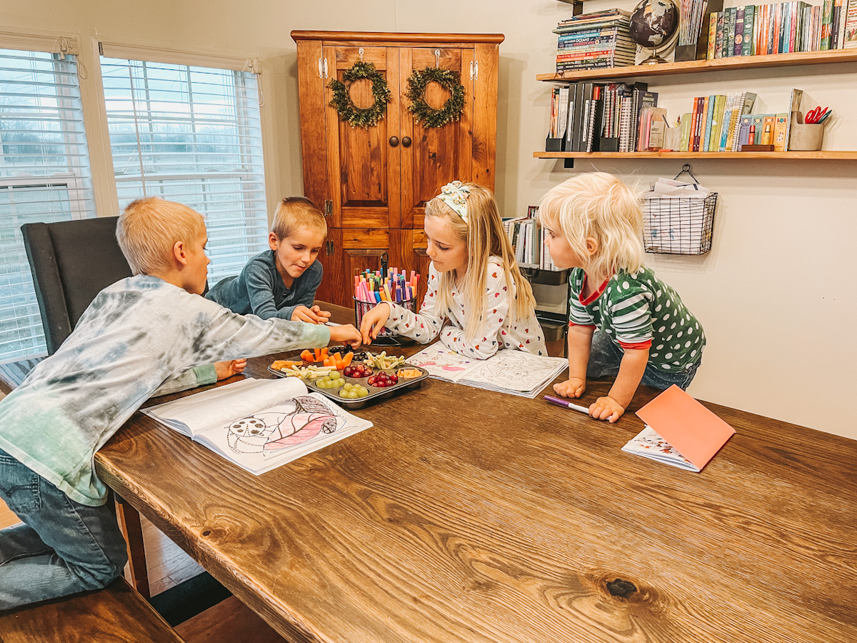 four kids sitting around the dining room table in their homeschool room, eating snacks and coloring during read aloud activities.