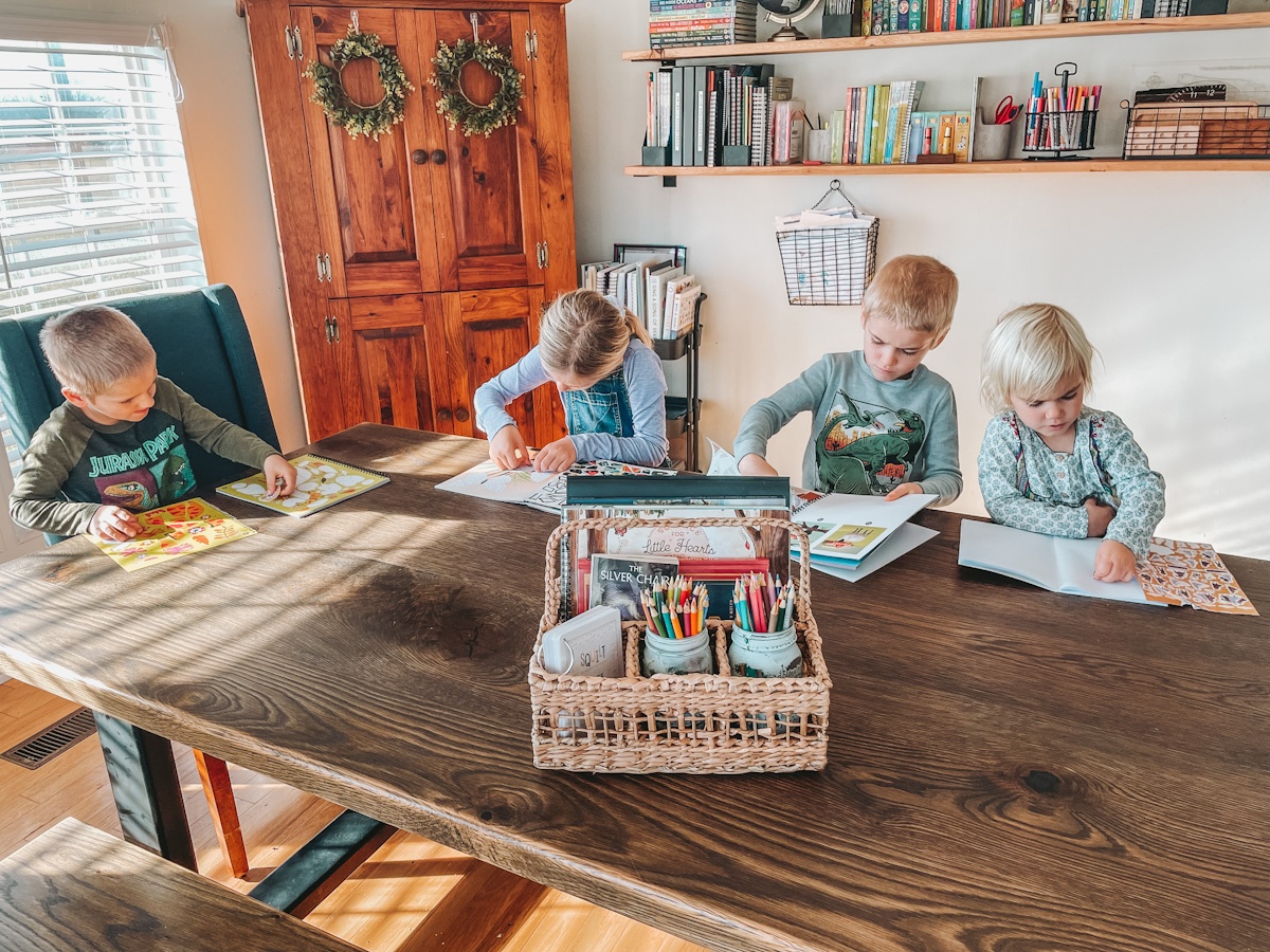 four kids sitting around a dining room table doing sticker books for their read aloud activity