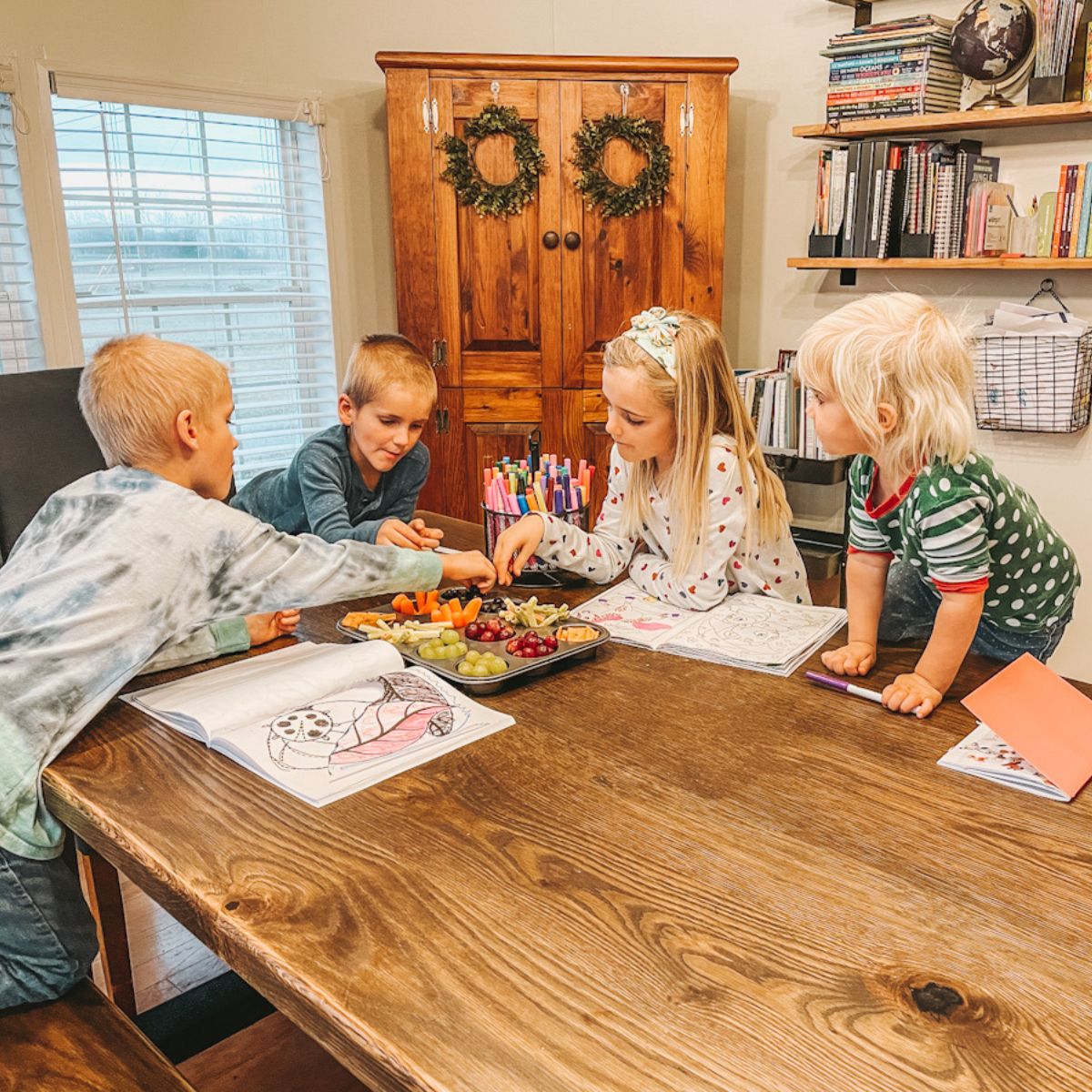 four kids sitting around the dining room table in their homeschool room, eating snacks and coloring during read aloud activities