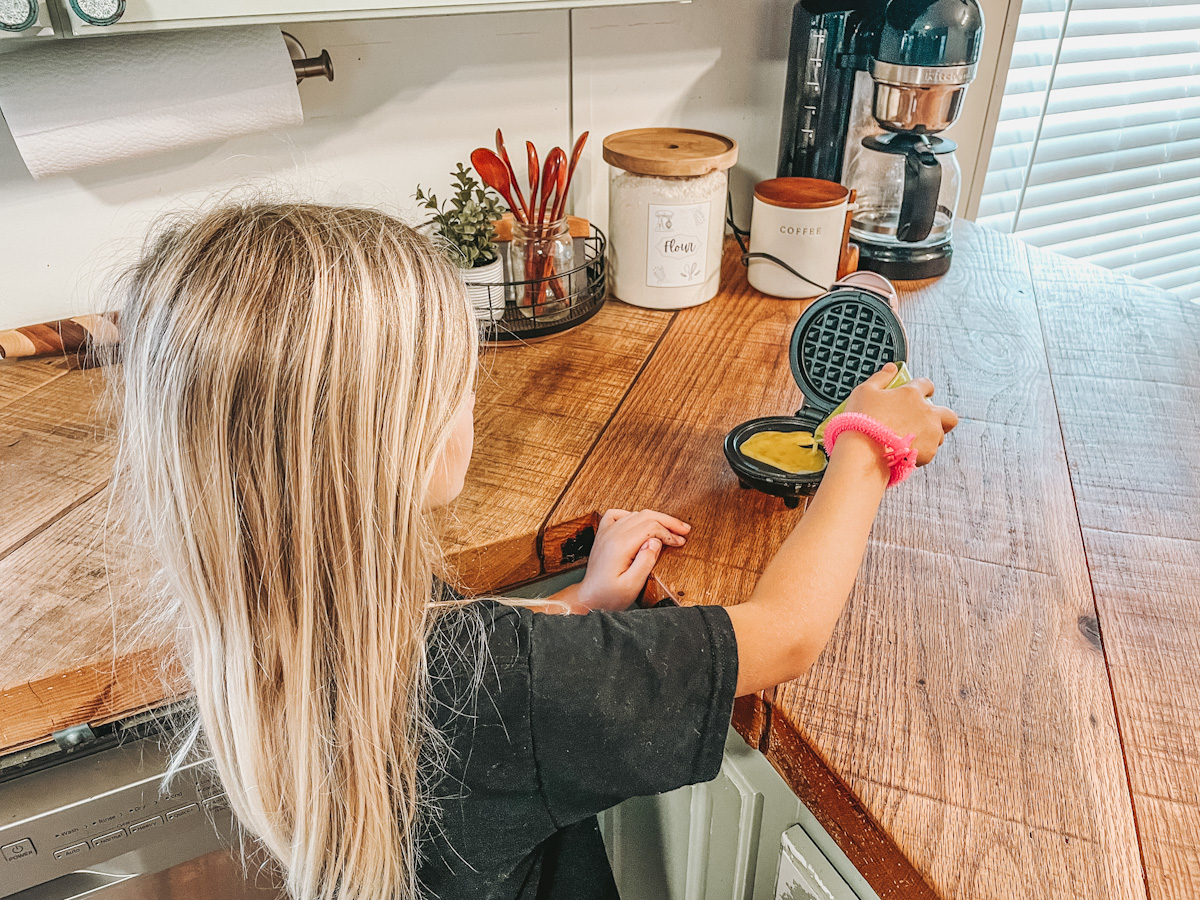 girl cooking eggs in a mini waffle maker for a simple homeschool breakfast idea