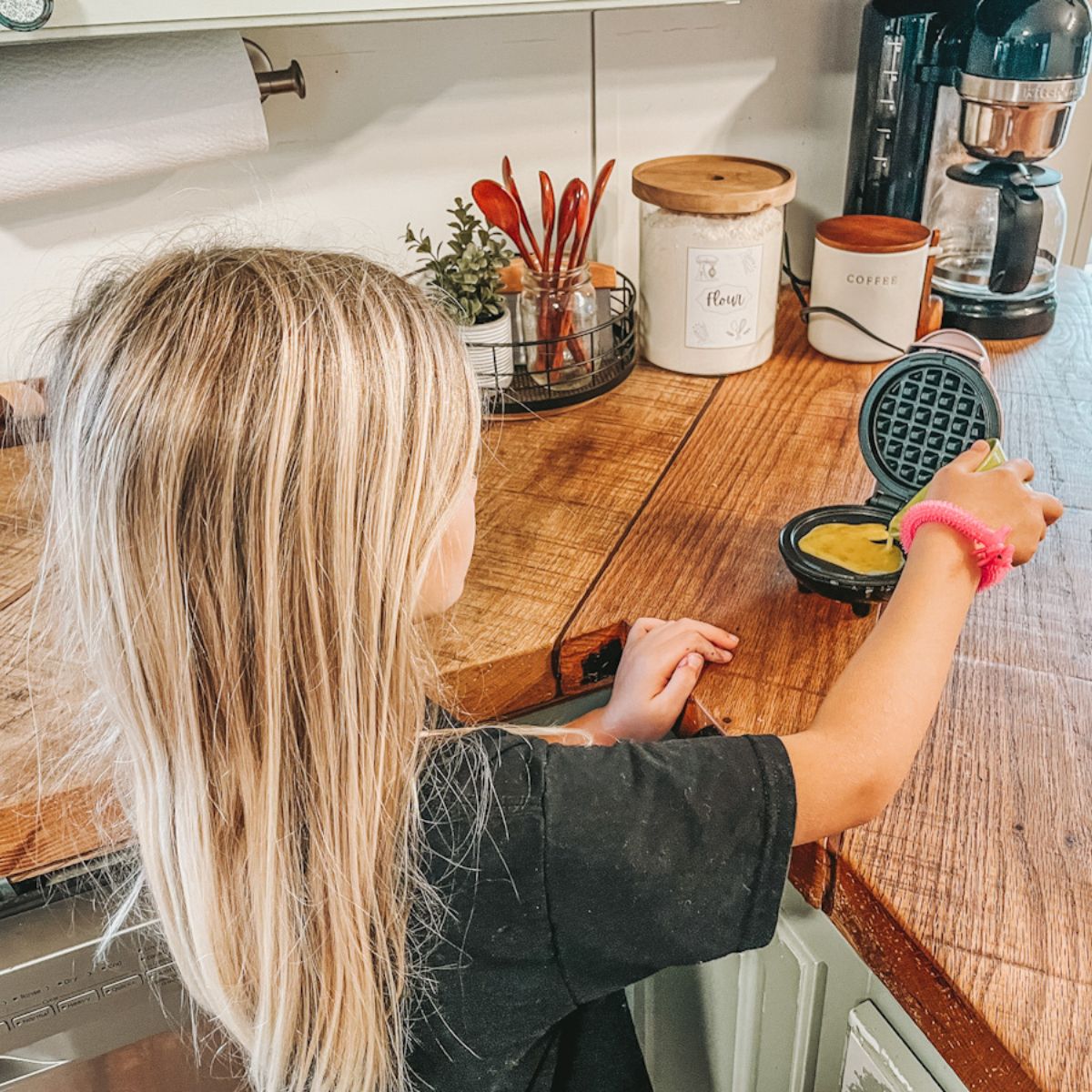 girl making eggs in a mini waffle maker for a simple homeschool breakfast idea