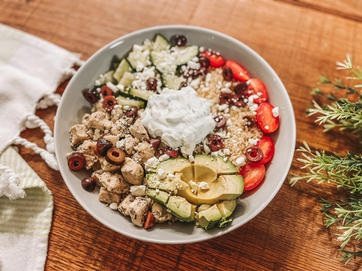 white bowl filled with grilled Greek chicken, quinoa, cucumber, avocado, cherry tomatoes, kalamata olives, feta, and Tzatziki