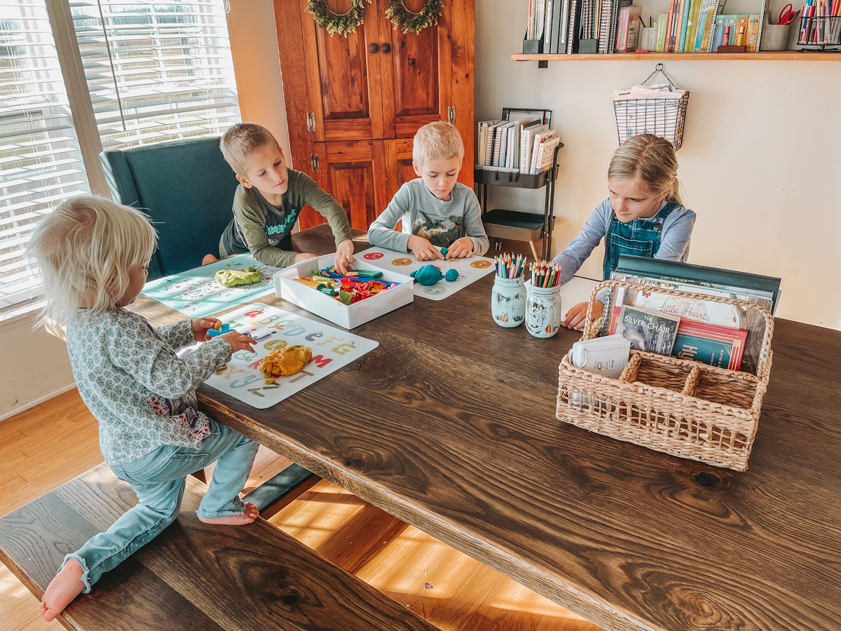 four homeschool kids gathered around the dining room table with playdoh to do some read aloud time
