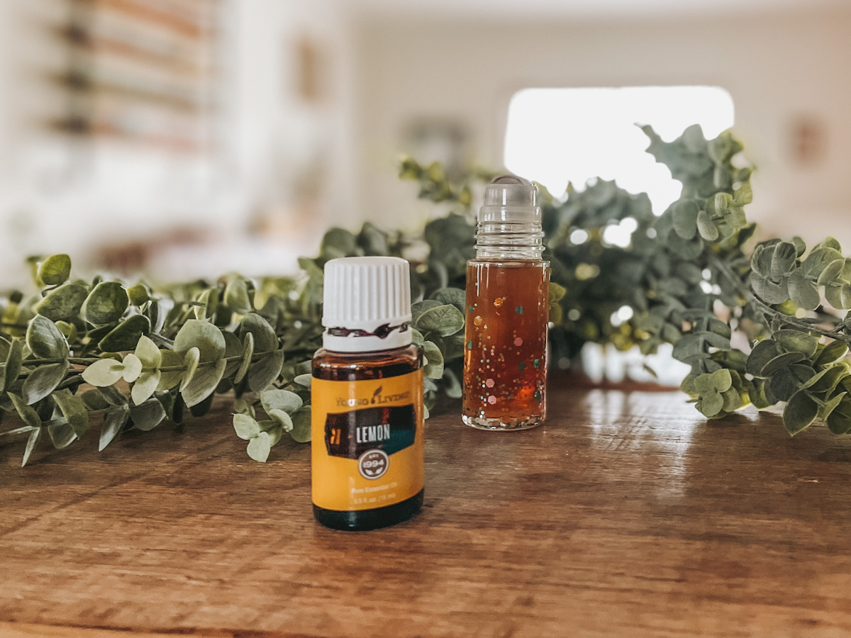 Lemon essential oil on a wood surface in front of a DIY laundry stain remover in a roller bottle