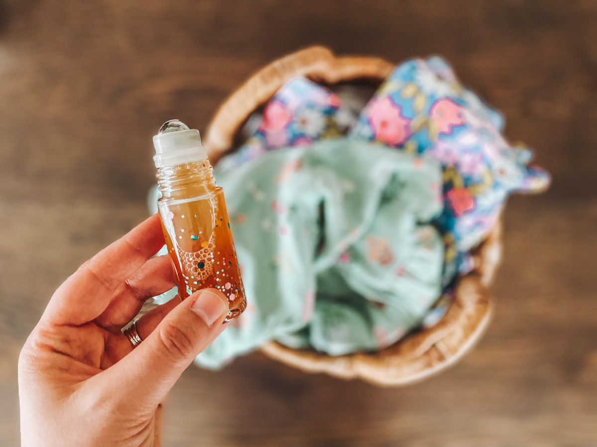 DIY laundry stain remover in a glass roller bottle held up in front of a laundry basket
