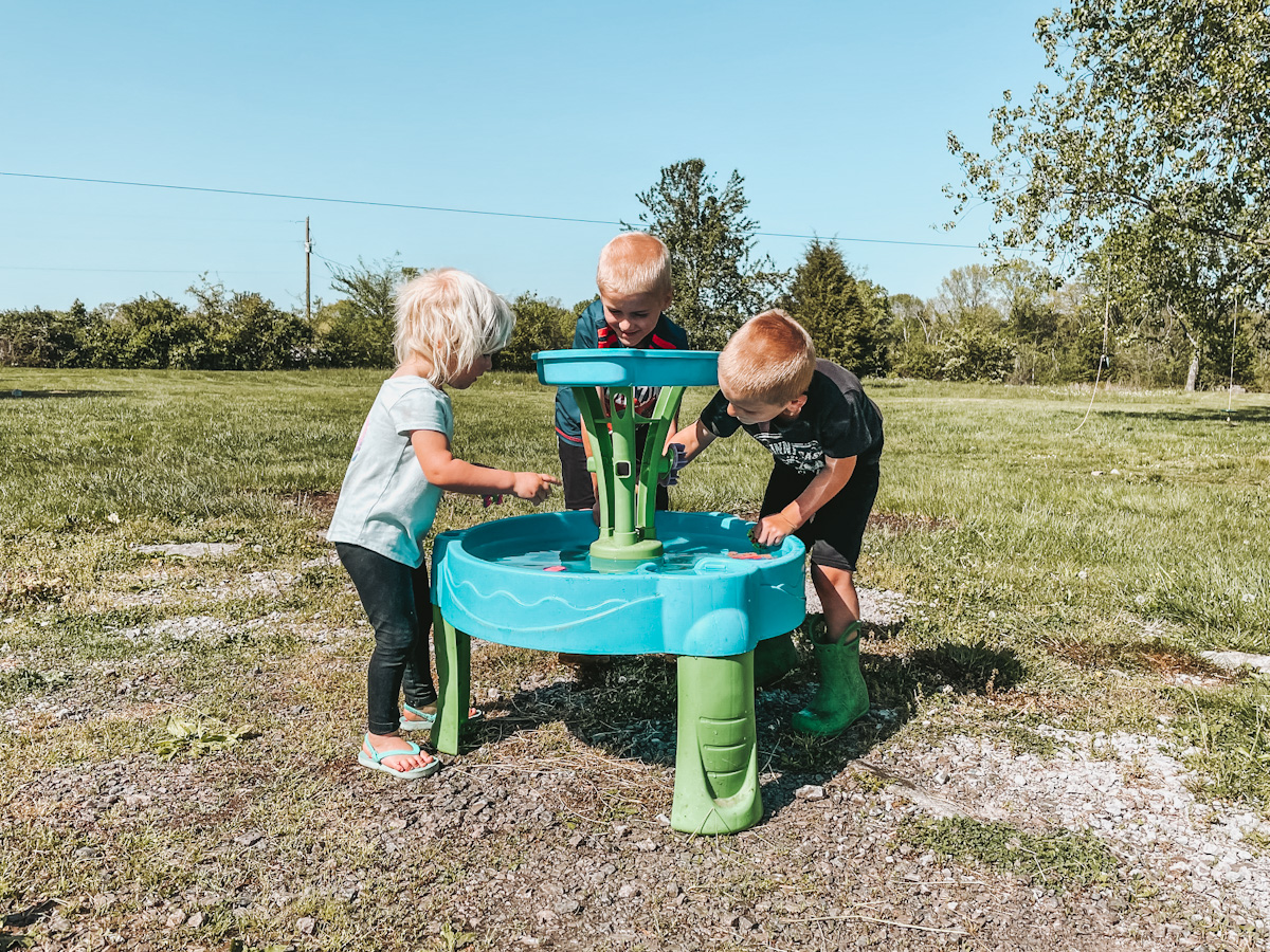 summer time water play with 3 kids around a blue water table during their homeschool schedule