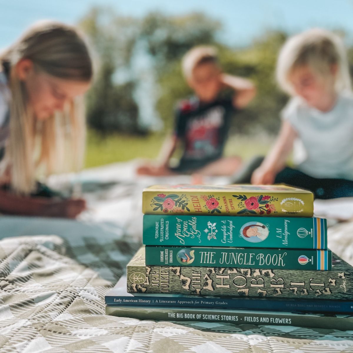 a book stack in front of 3 kids sitting on a picnic blanket drawing and coloring