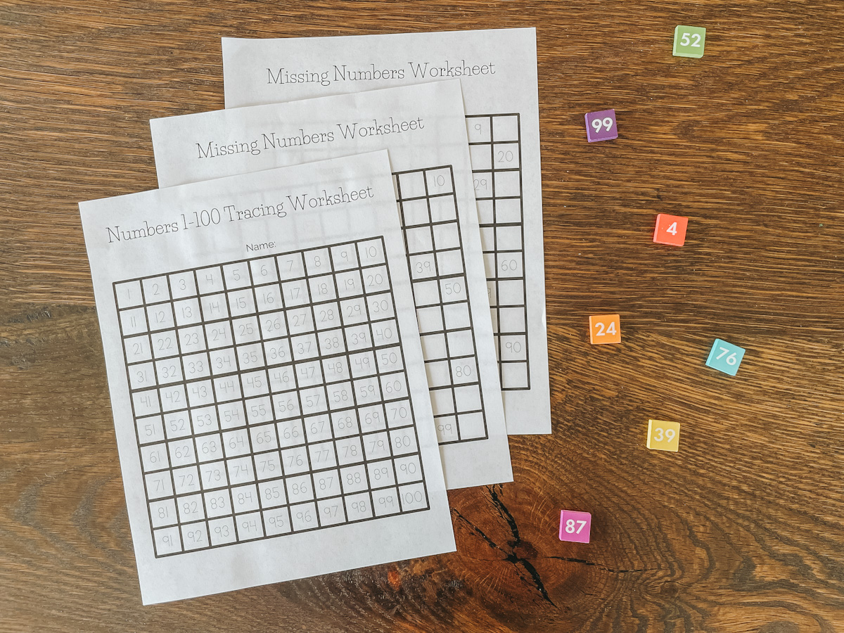 number tracing worksheets stacked up on a wood tabletop alongside colorful squares with numbers on them